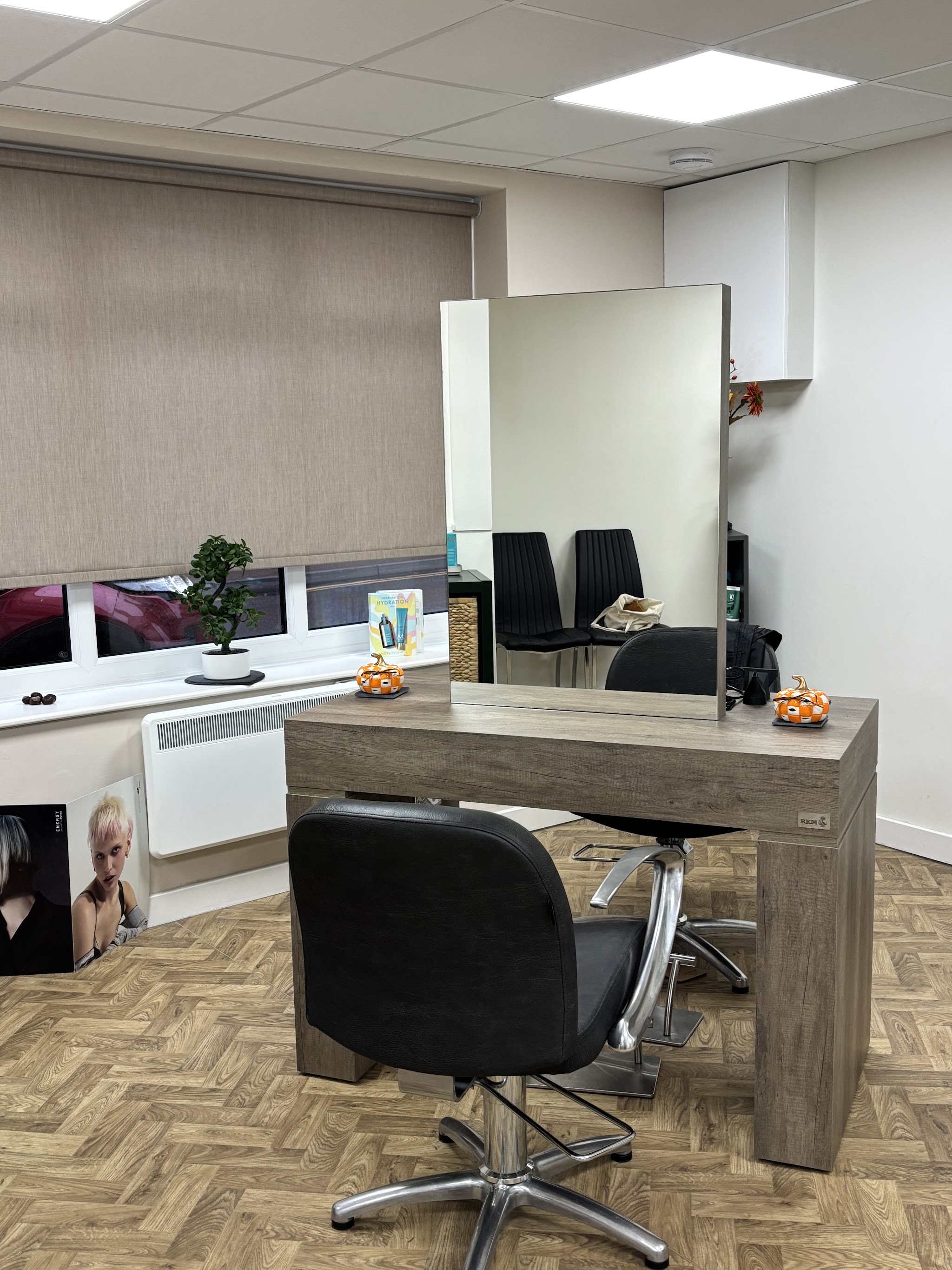Styling station with a large mirror and black salon chair on a herringbone floor