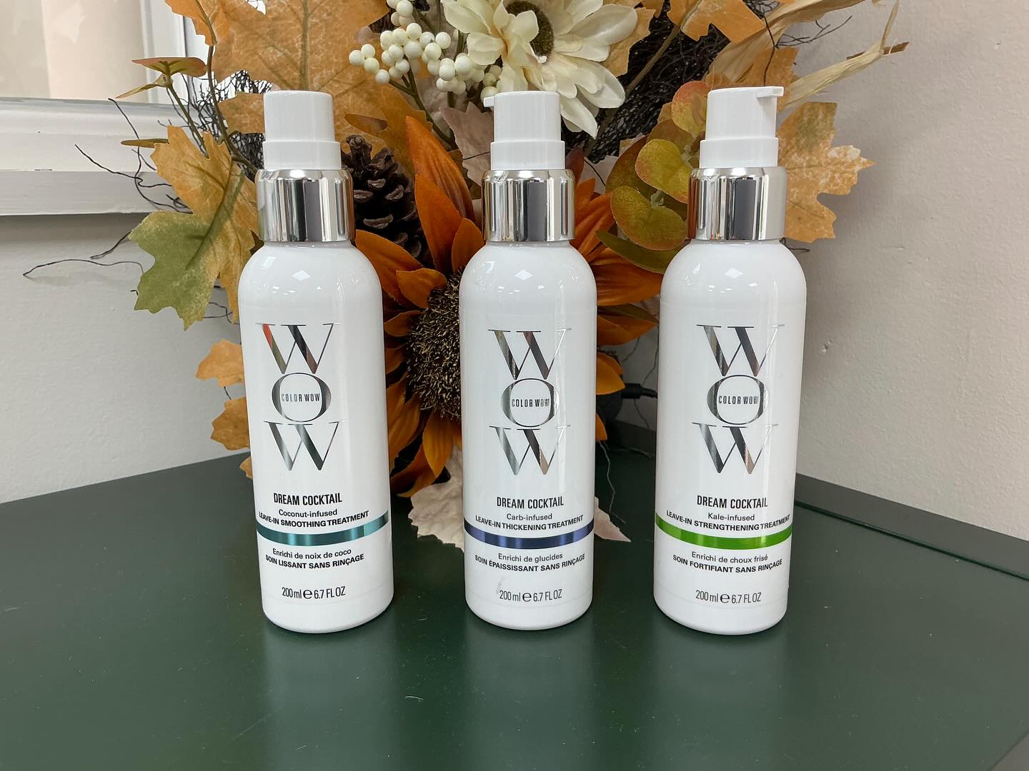 Three bottles of hair treatment on the green counter with autumn flowers